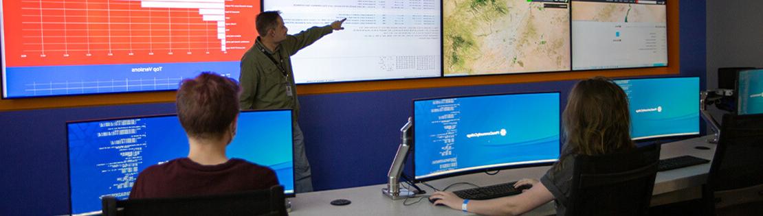 two students sit at computers in Pima's IT Center of Excellence listening to a teacher